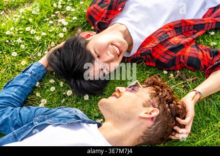 Coppie gay asiatiche e caucasiche che si guardano l'un l'altro sdraiati sull'erba nel parco durante il giorno Foto Stock