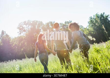 Donna nera con afro riccio che si guarda dietro la spalla camminando mano nella mano con amici caucasici e di corsa mista in campo nelle giornate di sole Foto Stock