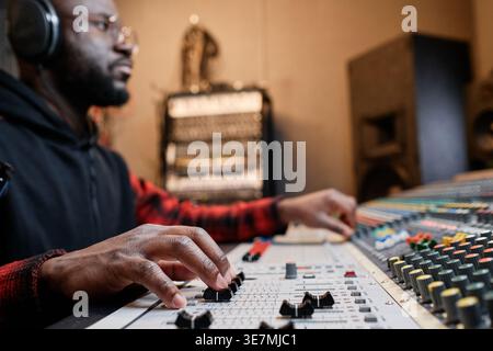Primo piano uomo nero calvo con occhiali e cuffie che lavorano al mixer nello studio di registrazione Foto Stock