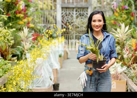 Donna asiatica che tiene l'erba con fiori in fiore in piedi in serra Foto Stock