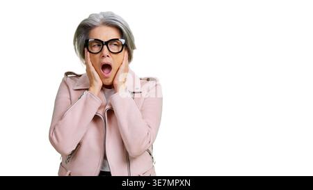 Donna anziana con occhiali e giacca rosa che reagisce al rumore Foto Stock