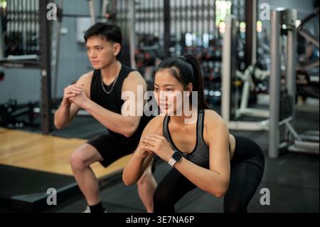 Uomo e donna asiatici che indossano abbigliamento sportivo che eseguono squat insieme in palestra Foto Stock
