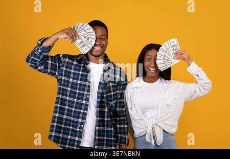 Coppia nera che copre gli occhi con i money mentre si trova su sfondo giallo in studio Foto Stock