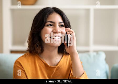 Ritratto di una donna araba sorridente che parla sul cellulare a casa, foto ravvicinata di una giovane donna mediorientale che ha una piacevole conversazione sul cellulare e. Foto Stock