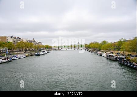 PARIGI, FRANCIA — 11 APRILE 2024: Vista panoramica della Senna con case galleggianti e navi turistiche ormeggiate lungo le rive vicino al Pont des Invalides. Foto Stock