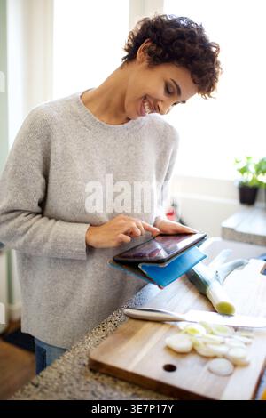Donna afroamericana sorridente che usa un tablet in piedi davanti al bancone della cucina Foto Stock