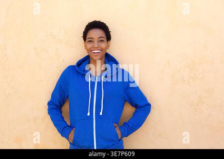 Donna afroamericana sorridente con le mani in tasca in piedi su sfondo beige Foto Stock