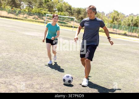 Sorridente coppia cinese di mezza età che gioca a calcio sul campo di calcio nelle giornate di sole Foto Stock