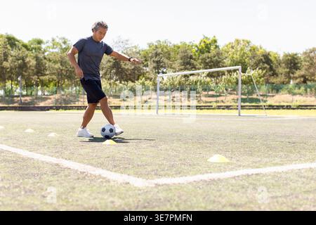Uomo cinese di mezza età che gioca a calcio in campo nelle giornate di sole Foto Stock