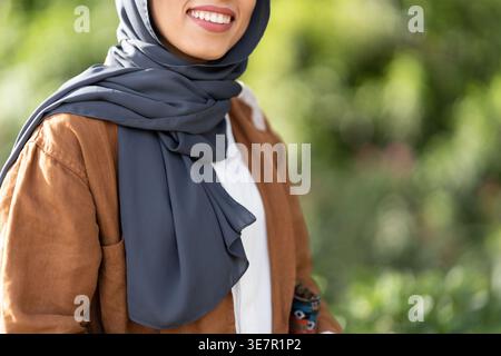 Donna musulmana sorridente in hijab in piedi nel parco durante il giorno Foto Stock