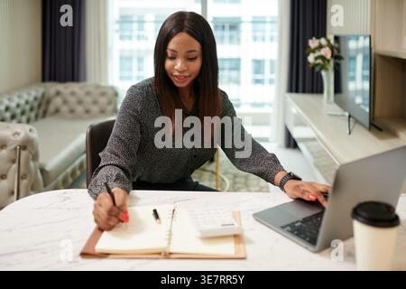 Donna nera che scrive appunti sul tavolo in salotto Foto Stock