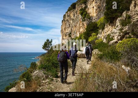 Escursionisti su un sentiero costiero nella Riviera di Ulisse in Italia. Sperlonga, Italia - 15 marzo 2026: Un gruppo di escursionisti segue uno stretto sentiero roccioso lungo le scogliere calcaree. L'immagine documenta la rete di sentieri all'aperto all'interno del Parco regionale e la tipica macchia mediterranea della costa laziale. Sperlonga Latina Italia Copyright: XGennaroxLeonardix Foto Stock