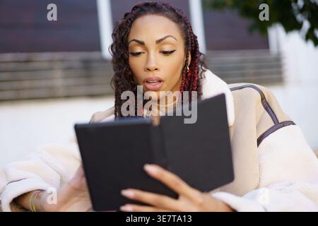 Donna nera con trecce che usa un tablet seduto in un ristorante all'aperto Foto Stock