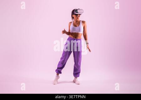 Donna nera che indossa occhiali di protezione per la realtà virtuale su sfondo viola in studio Foto Stock
