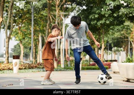 Padre asiatico che gioca a calcio con il figlio nel parco Foto Stock