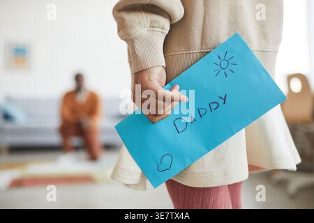 Primo piano di Black girl che tiene una lettera per suo padre per il giorno di FatherÂ mentre si trova in salotto di casa Foto Stock