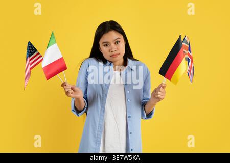 Adolescente asiatica che tiene bandiere mentre si trova su sfondo giallo in studio Foto Stock