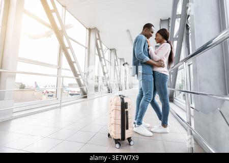 Una coppia di persone di colore con una valigia rivolta l'una di fronte all'altra in piedi sul passaggio pedonale dell'aeroporto Foto Stock
