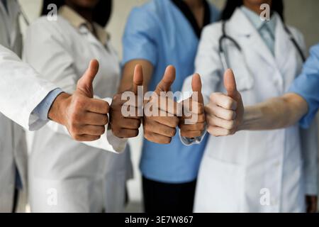 Immagine ritagliata di diversi gruppi di medici in uniformi che mostra pollice su mentre si sta in piedi insieme in ospedale Foto Stock