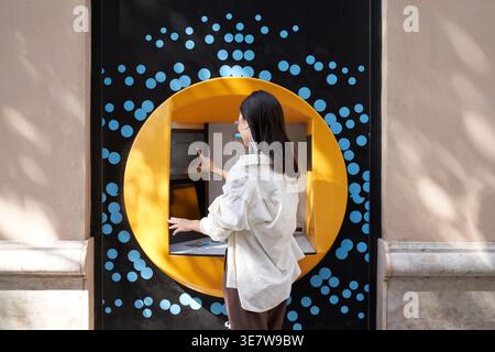 Donna giapponese in piedi per strada e ritirare soldi dal bancomat durante il giorno Foto Stock