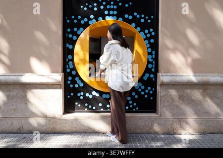 Donna giapponese in piedi per strada e ritirare soldi dal bancomat durante il giorno Foto Stock