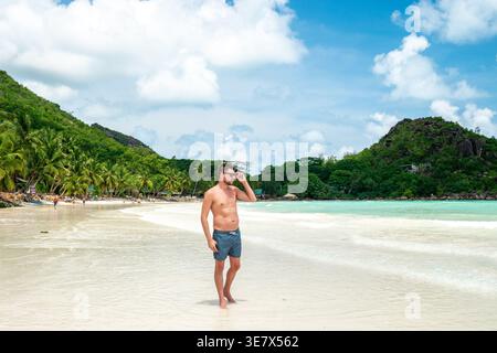 Un viaggiatore passeggia lungo la splendida costa delle Seychelles, circondato da acque cristalline e da una vegetazione lussureggiante. Le onde scivolano delicatamente sulla sabbia soffice, creando un paradiso perfetto per le vacanze. Foto Stock