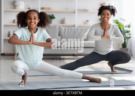 Madre e figlia di colore con le mani di preghiera che praticano l'esercizio yoga sul tappetino yoga nel soggiorno di casa Foto Stock