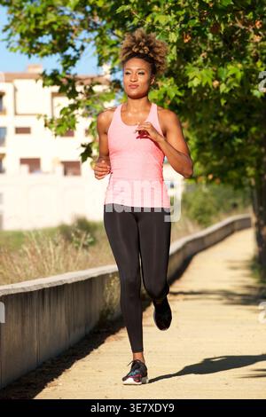 Donna nera con acconciatura afro bionda che corre all'aperto nelle giornate di sole Foto Stock