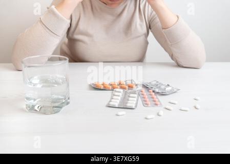Primo piano di farmaco sul tavolo con un bicchiere d'acqua e persona stressata, concetto di assistenza sanitaria Foto Stock
