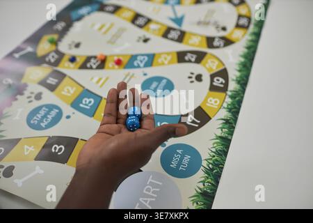 Mani di nero che tengono i dadi mentre si trova a tavola con un gioco da tavolo nella biblioteca del college Foto Stock