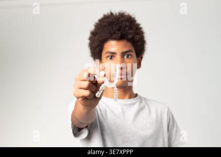 Adolescente cubano con afro che tiene in mano due allineatori dentali chiari su sfondo bianco in studio Foto Stock
