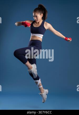 Donna cinese in mano che salta su sfondo blu in studio Foto Stock