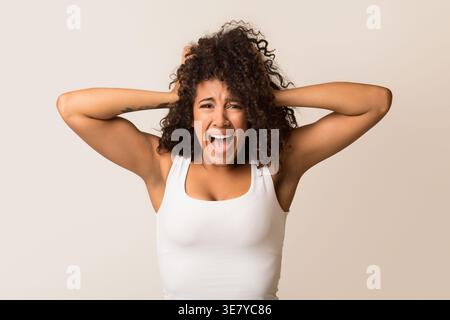 Donna nera scioccata con capelli ricci in piedi su sfondo chiaro in studio Foto Stock