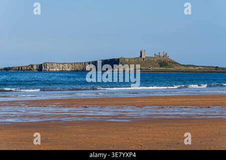 Castello medievale in rovina su un promontorio con scogliere spettacolari, visto da una spiaggia sabbiosa con dolci onde che lambiscono la riva Foto Stock