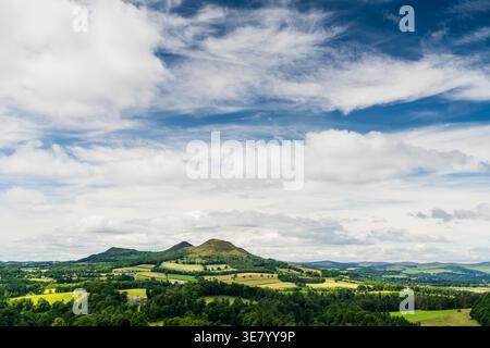 Un'ampia vista di campagna verdeggiante con colline ondulate e un cielo dinamico pieno di nuvole bianche e macchie blu Foto Stock