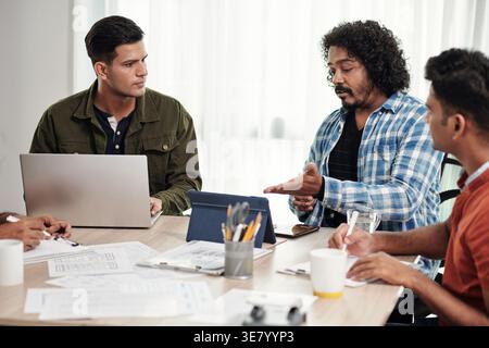 Programmatori indiani maschi seduti a un tavolo usando un computer portatile e un tablet che discutono di nuove idee che lavorano insieme in ufficio Foto Stock