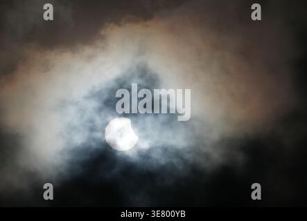 Una vista suggestiva del sole parzialmente oscurata dalla luna durante un'eclissi, sullo sfondo di nuvole vorticose e suggestive Foto Stock