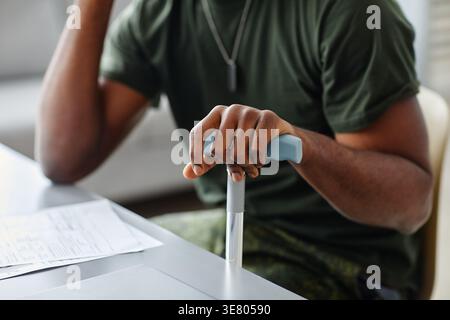 Mani di un militare nero che tiene il bastone seduto al tavolo in clinica Foto Stock