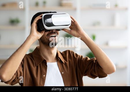 Uomo del Medio Oriente che indossa occhiali VR e sperimenta la realtà virtuale mentre è a casa Foto Stock