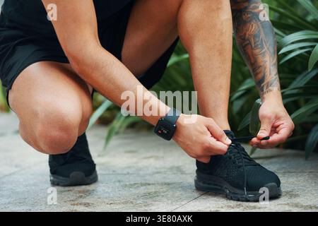 Uomo asiatico che lega lacci di scarpe mentre accovacciano all'aperto durante il giorno Foto Stock