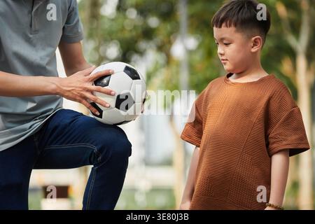 Ragazzo asiatico che impara il calcio con il padre nel parco Foto Stock