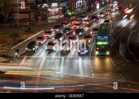 Una scena stradale trafficata a Seoul, Corea del Sud, di notte. Numerose auto e un autobus vengono catturati in movimento, con i fari accesi. Foto Stock