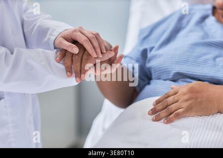 Immagine ravvicinata della mano della donna di mezza età nera tenuta da un medico donna in stanza d'ospedale Foto Stock