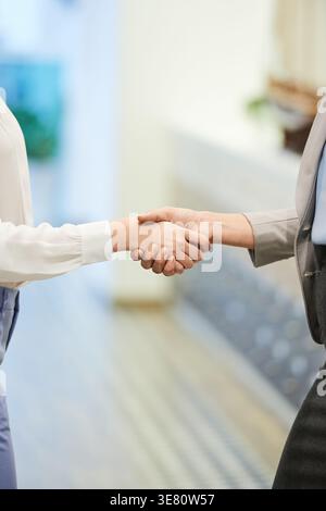 Immagine ritagliata di diverse donne d'affari che stringono la mano mentre si trovano in corridoio dell'ufficio Foto Stock