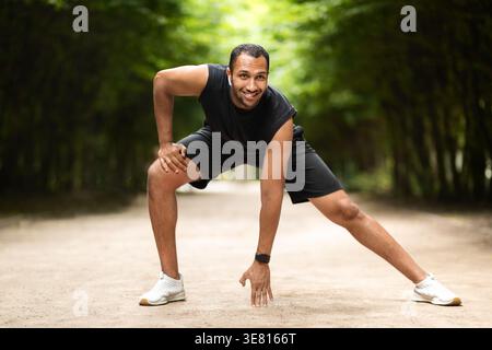 Uomo di colore che indossa abbigliamento sportivo e auricolari che si allenano all'aperto durante il giorno Foto Stock