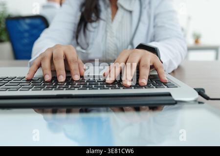 Donna indiana medico che digita sul computer portatile seduto alla scrivania in ufficio Foto Stock
