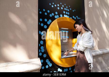 Donna giapponese in piedi per strada e ritirare soldi dal bancomat durante il giorno Foto Stock