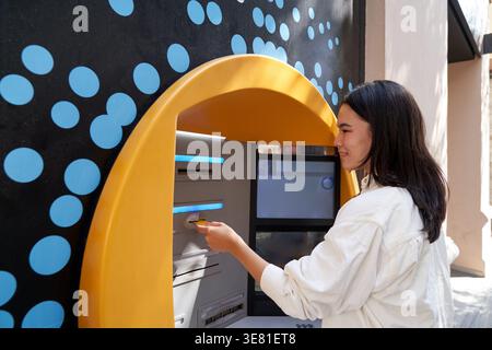 Donna giapponese in piedi per strada e ritirare soldi dal bancomat durante il giorno Foto Stock