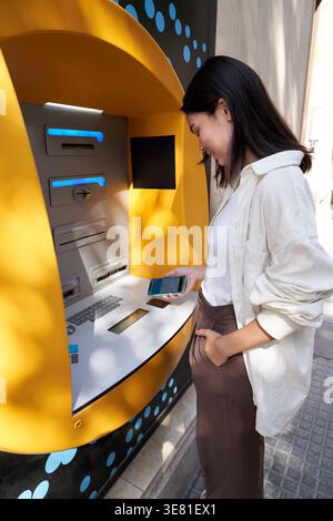 Donna giapponese in piedi per strada e ritirare soldi dal bancomat durante il giorno Foto Stock