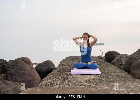 Donna ispanica in abbigliamento sportivo che pratica yoga sul molo sul lungomare durante il giorno Foto Stock